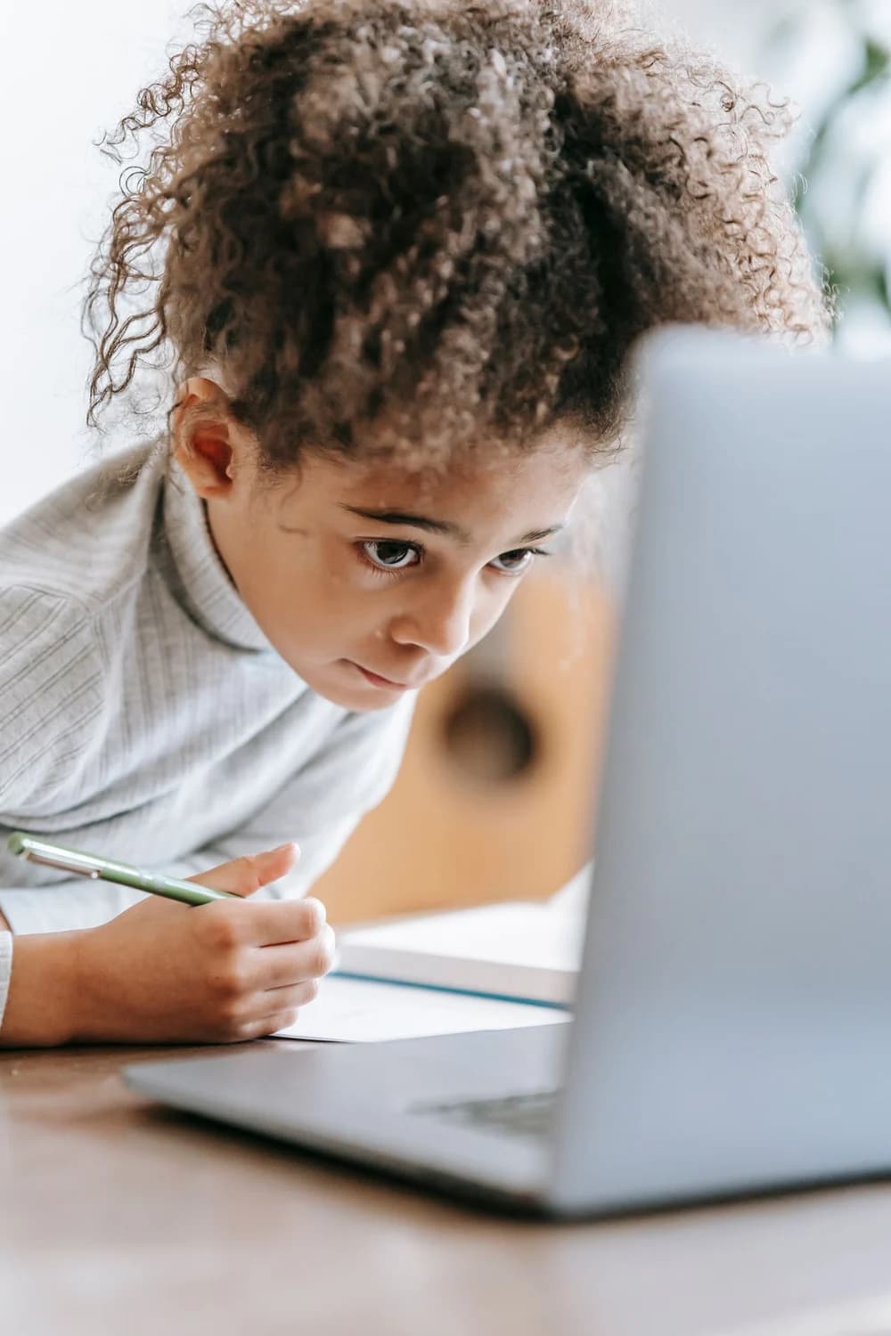 A young learner taking notes beside her laptop